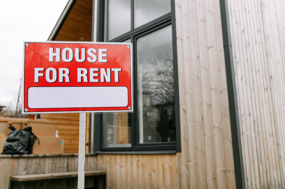 Red house for rent sign in front of a wooden house