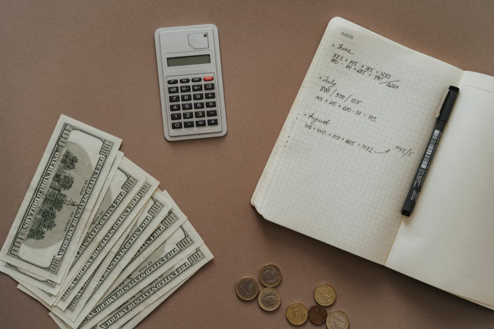 Note book with scribbles, pocket calculator, coins, and money bills